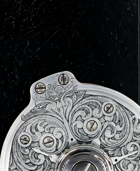 Close up of a Hand engraved salar fly fishing reel by VRDesigns. The engraving features scrollwork. The reel is sitting on a black background