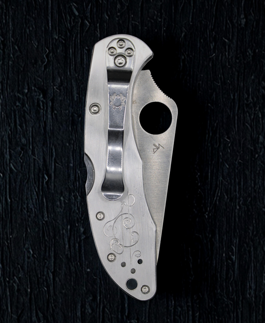 Silver folding knife with engraved design on a black textured background