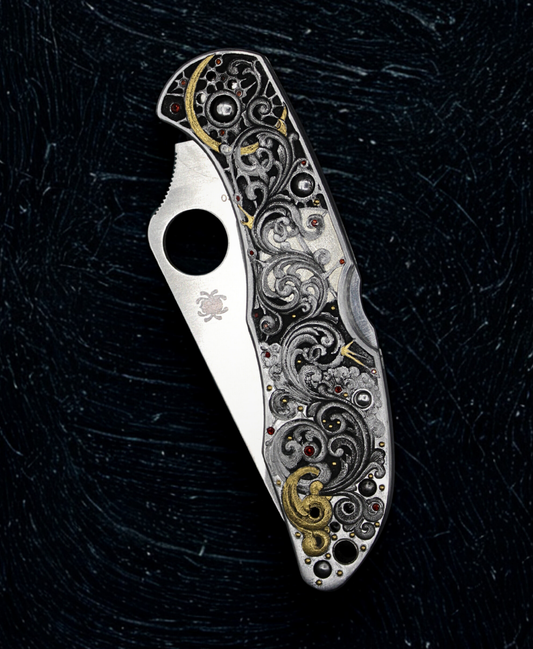 Hand engraved folding knife. The folding knife features scrollwork with gold and silver inlay and garnet stones.