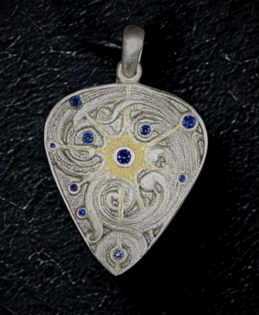 Hand engraved silver pendant with a gold inlay star in the middle. There is engraved scrollwork in the star. A sapphire is in the center of the star, the star is surrounded by sapphires.