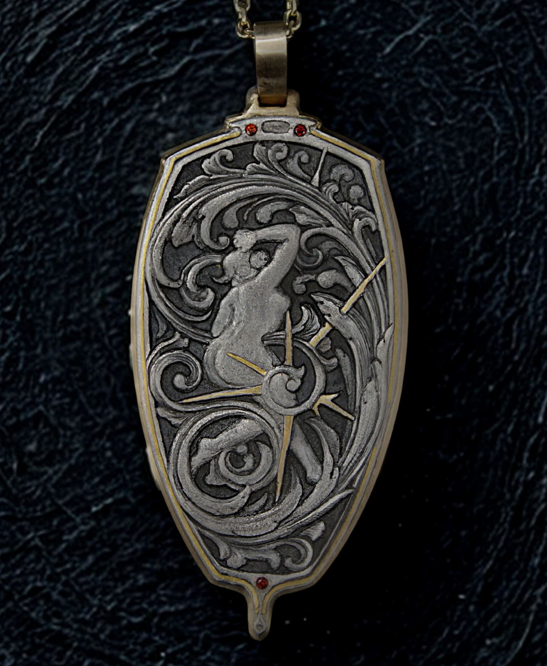 Hand engraved silver pendant with a gold frame. The pendant features scrollwork and a figure in the center. It features 3 garnets and is on a black background.