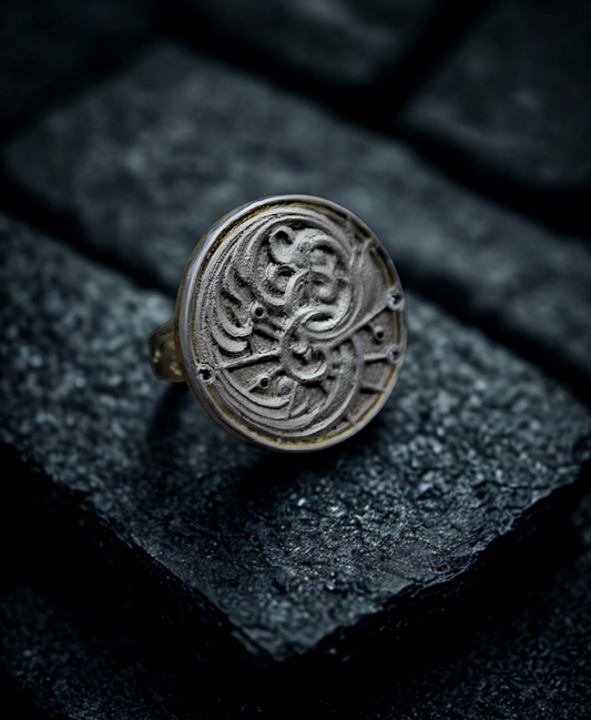 Hand made and hand engraved two tone ring. The ring features a yellow gold shank, with a silver and gold disc shape top. The top has scrollwork engraving and scattered sapphires. It is on a black background.