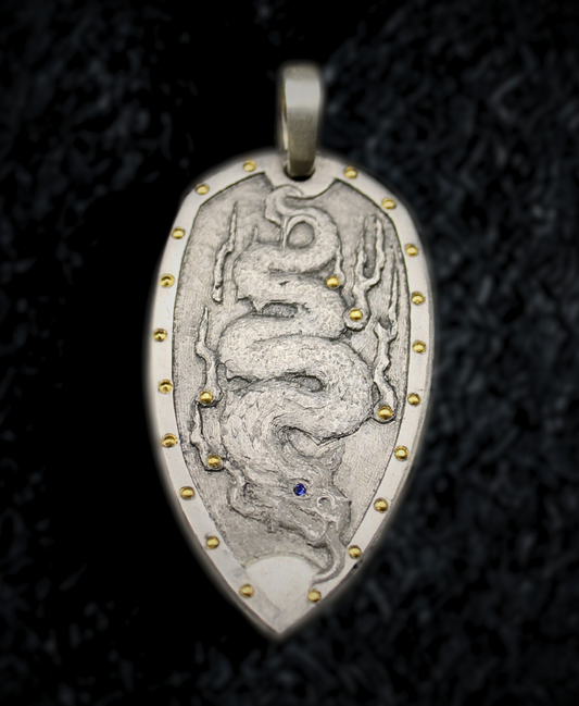 Silver pendant with engraved design on a dark textured background