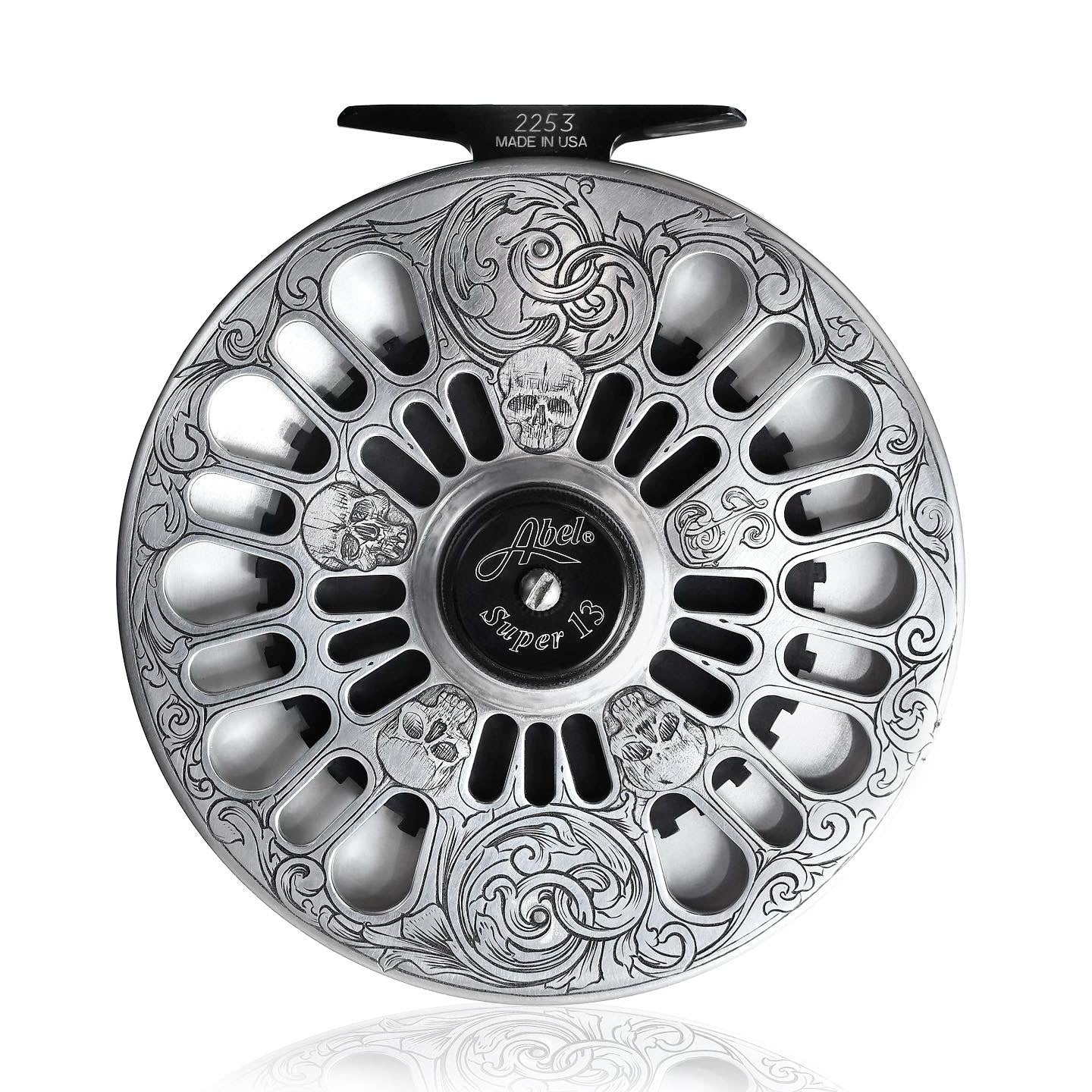 Silver fishing reel with intricate designs on a white background