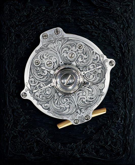 Hand engraved salar fly fishing reel by VRDesigns. The engraving features scrollwork. The reel is sitting on a black background.