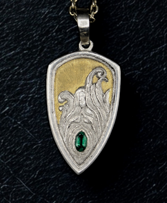 Decorative pendant with intricate design and green gemstone on a black background with a female in the center.